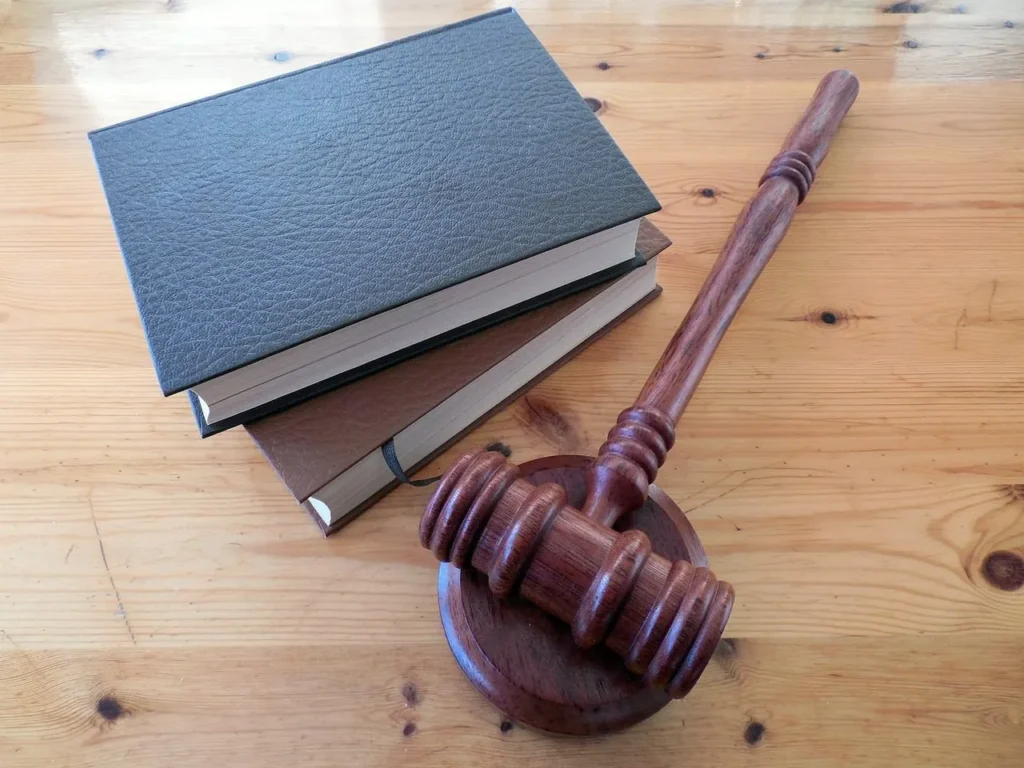 A gavel and a stack of law books placed on a wood table.