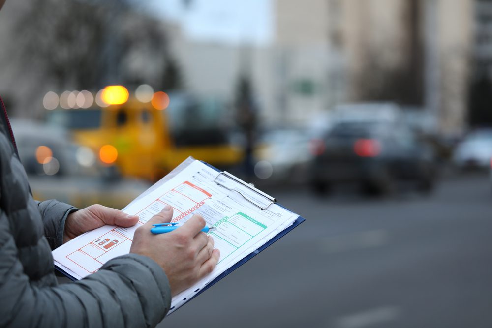 A insurance adjuster inspecting a car accident, holding a clip board with a checklist of items.