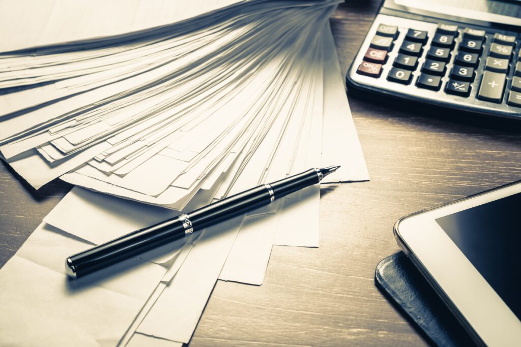 A stack of documents on a table with a fountain pen and a calculator.