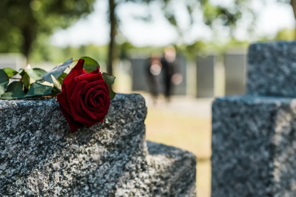 A grave headstone with a red rose laid on top.