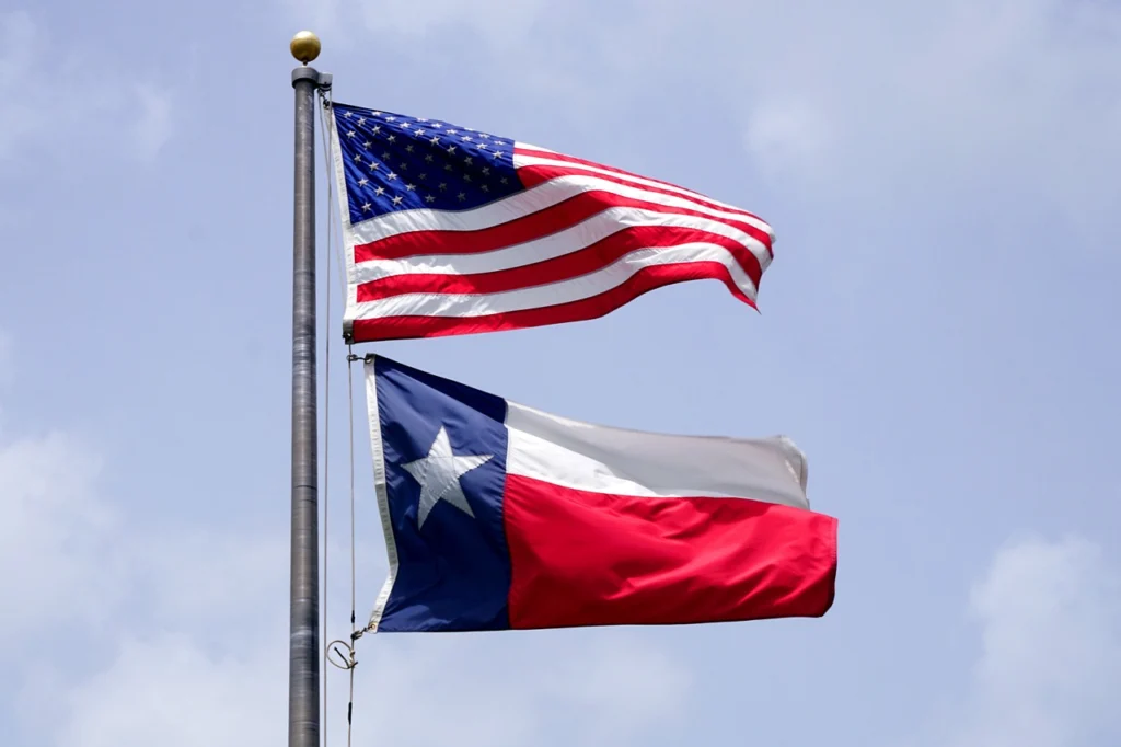The flag of the United States of America and the state flag of Texas, flying proudly from a flag pole.