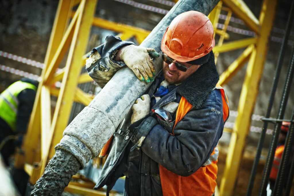 A construction worker carrying a large concrete pipe.