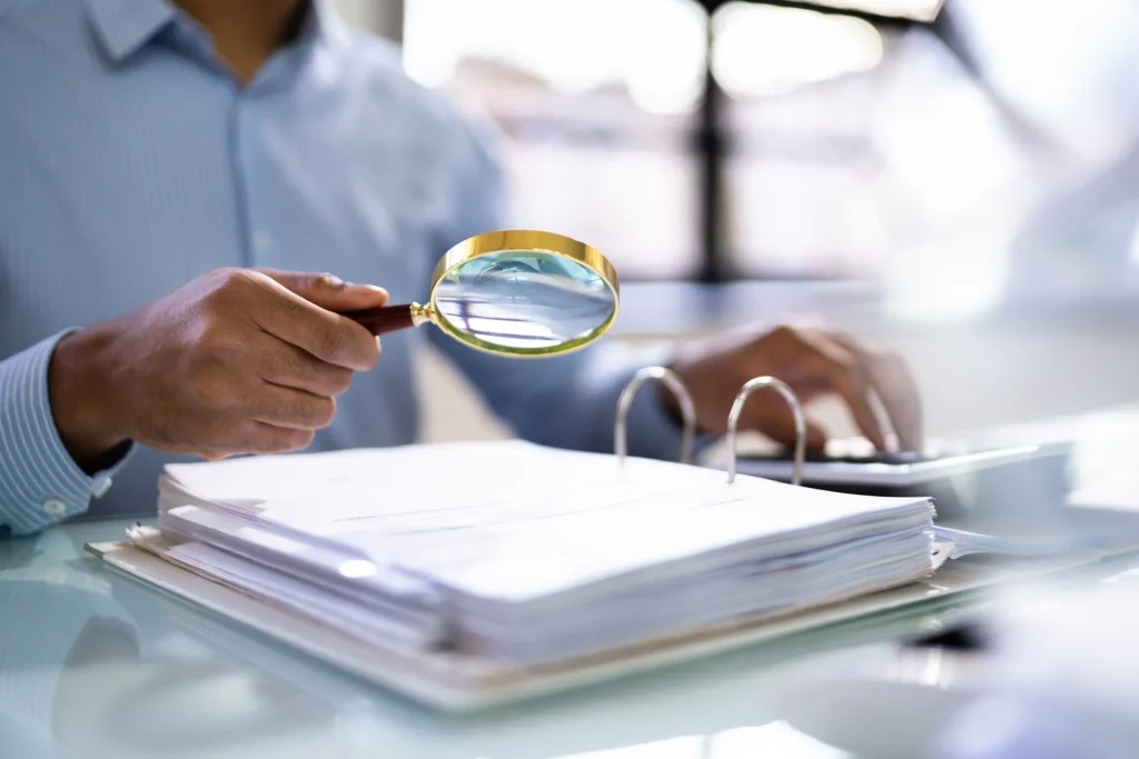 A lawyer looking through documents in a binder using a magnifying glass,